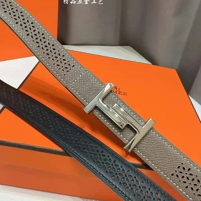 Grey perforated belt with a metal buckle displayed on an orange box