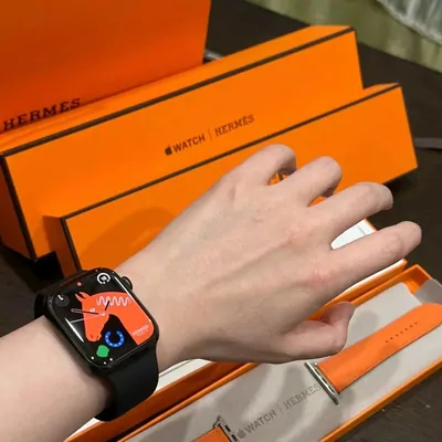 Wrist wearing a dark smart-style watch beside orange boxes